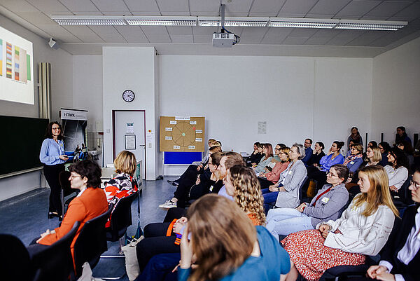 Professorin Graßmann steht vor dem Publikum und hält eine Keynote. Im Hintergrund auf der Wand ist ihre Powerpoint-Präsentation zu sehen.