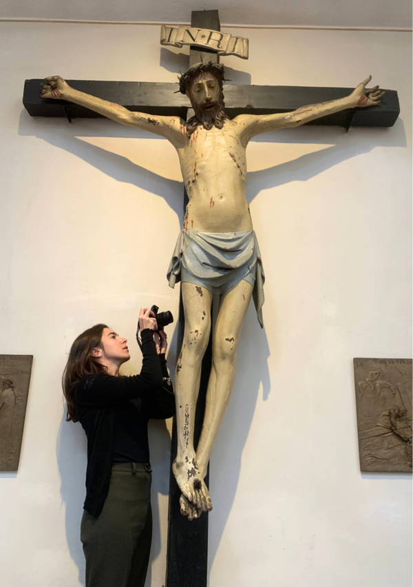 Arianna Favaretto Cortese Ein bewegliches Kruzifix mit einer Skulptur von Christus. Daneben eine Frau, die das Kunstwerk fotografiert.