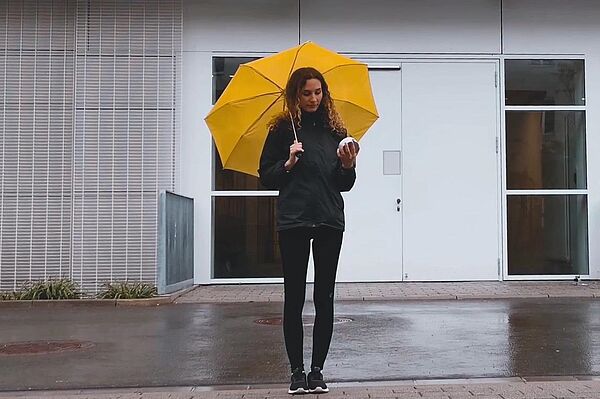 Eine Frau steht vor einem Gebäude mit einem gelben Regenschirm in der Hand.