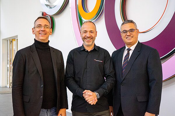 (v. l. n. r.): Prof. Andreas Both, Martin Flechsig, Prof. Faouzi Derbel/Kooperation drei Herren im anzug vor einem Kunsterk lachen in die Kamera