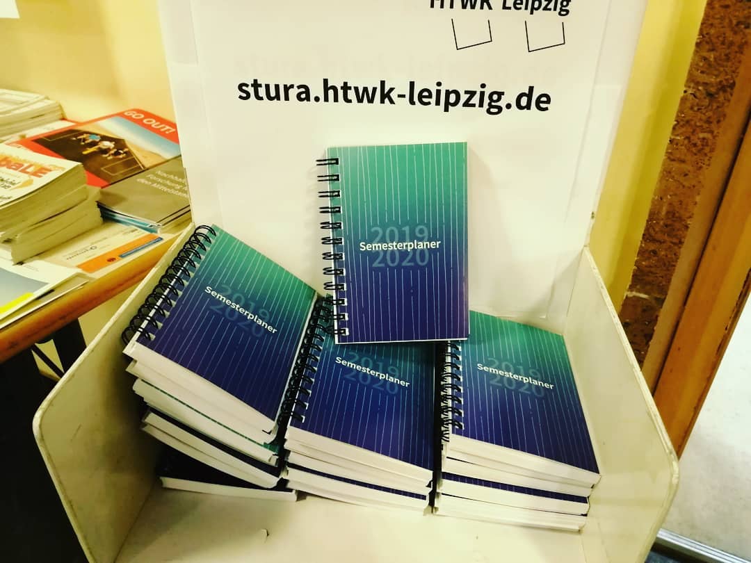 Die Semesterplaner „Eins.Null” des StuRa liegen vor dem Büro in einem Flyerständer.